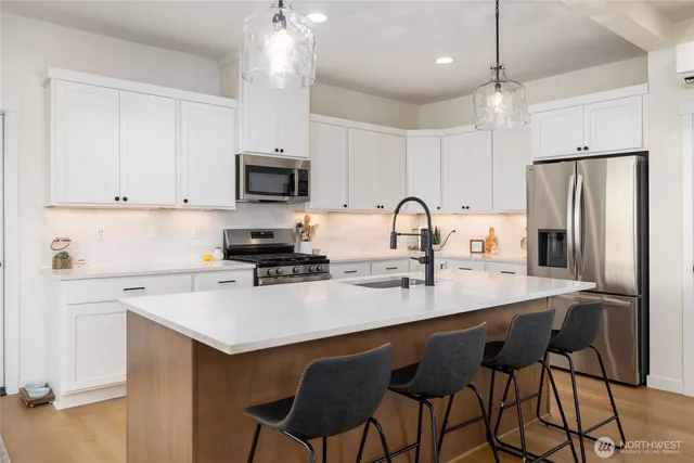 a kitchen with stainless steel appliances a stove a refrigerator sink and white cabinets with wooden floor