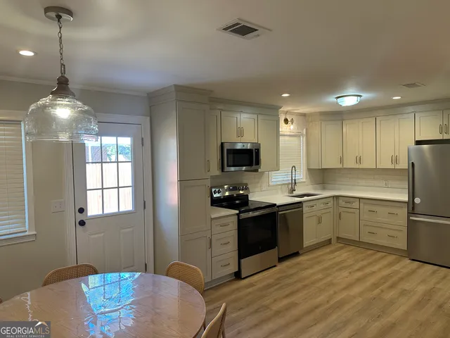 a kitchen with stainless steel appliances granite countertop a stove top oven a sink dishwasher a refrigerator and a dining table with wooden floor