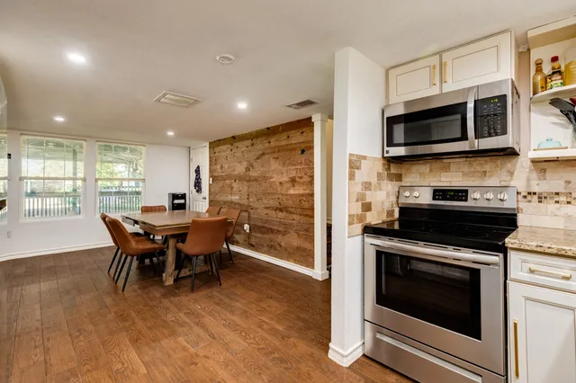 a kitchen with stainless steel appliances granite countertop a stove top oven a sink dishwasher a dining table and chairs with wooden floor