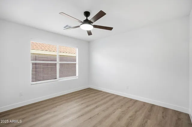 an empty room with wooden floor ceiling fan and windows