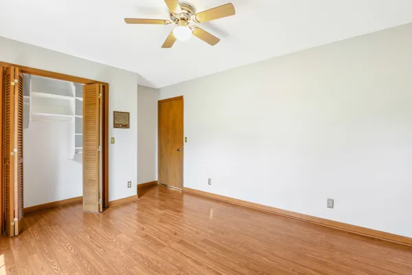an empty room with wooden floor closet and windows