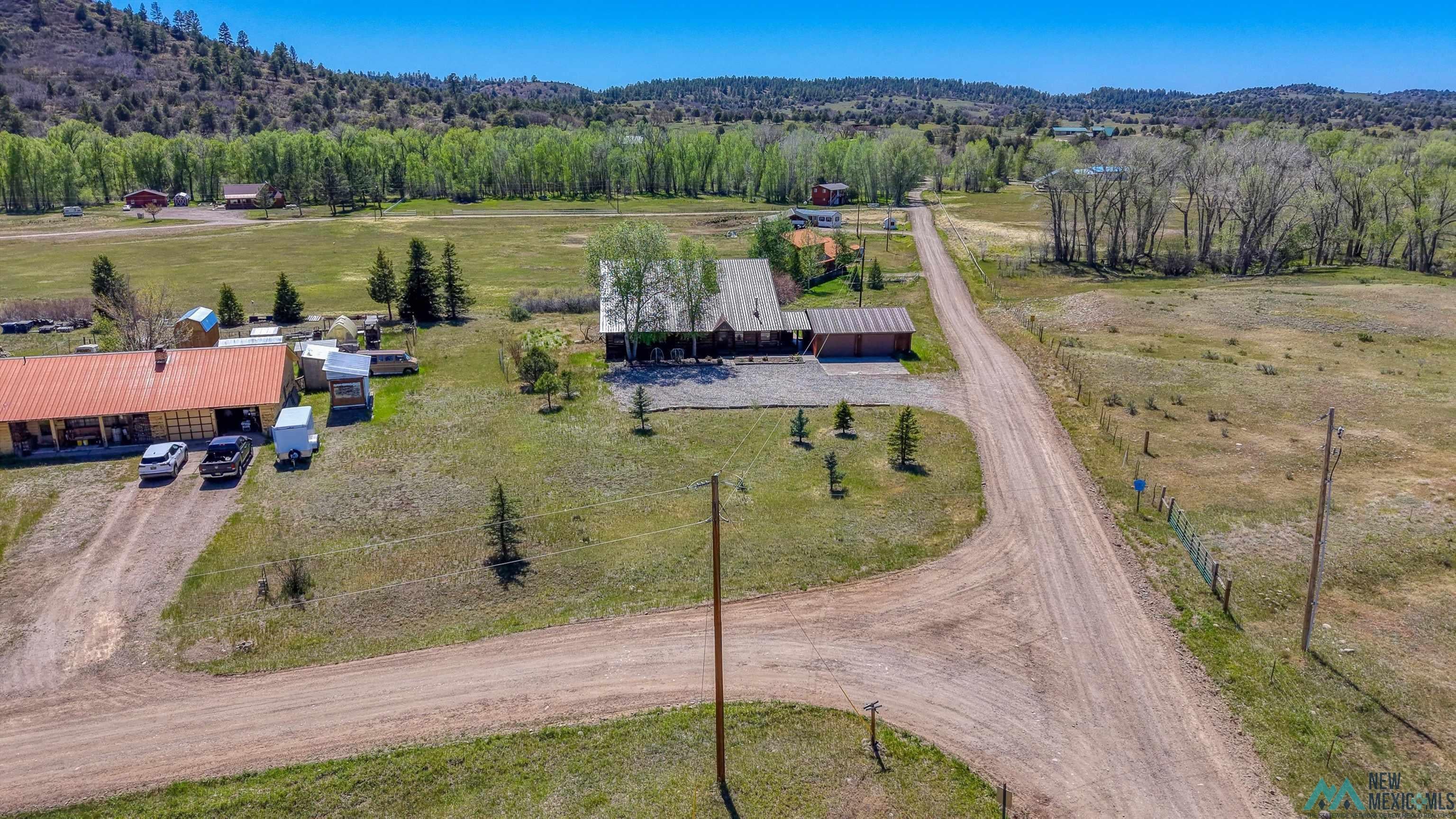 83 Juniper Road Chama, NM 87520 - Photo 51 of 56 Expansive property featuring multiple structures, a main residence with an attached garage, a secondary long building with a red roof, and a gravel driveway system