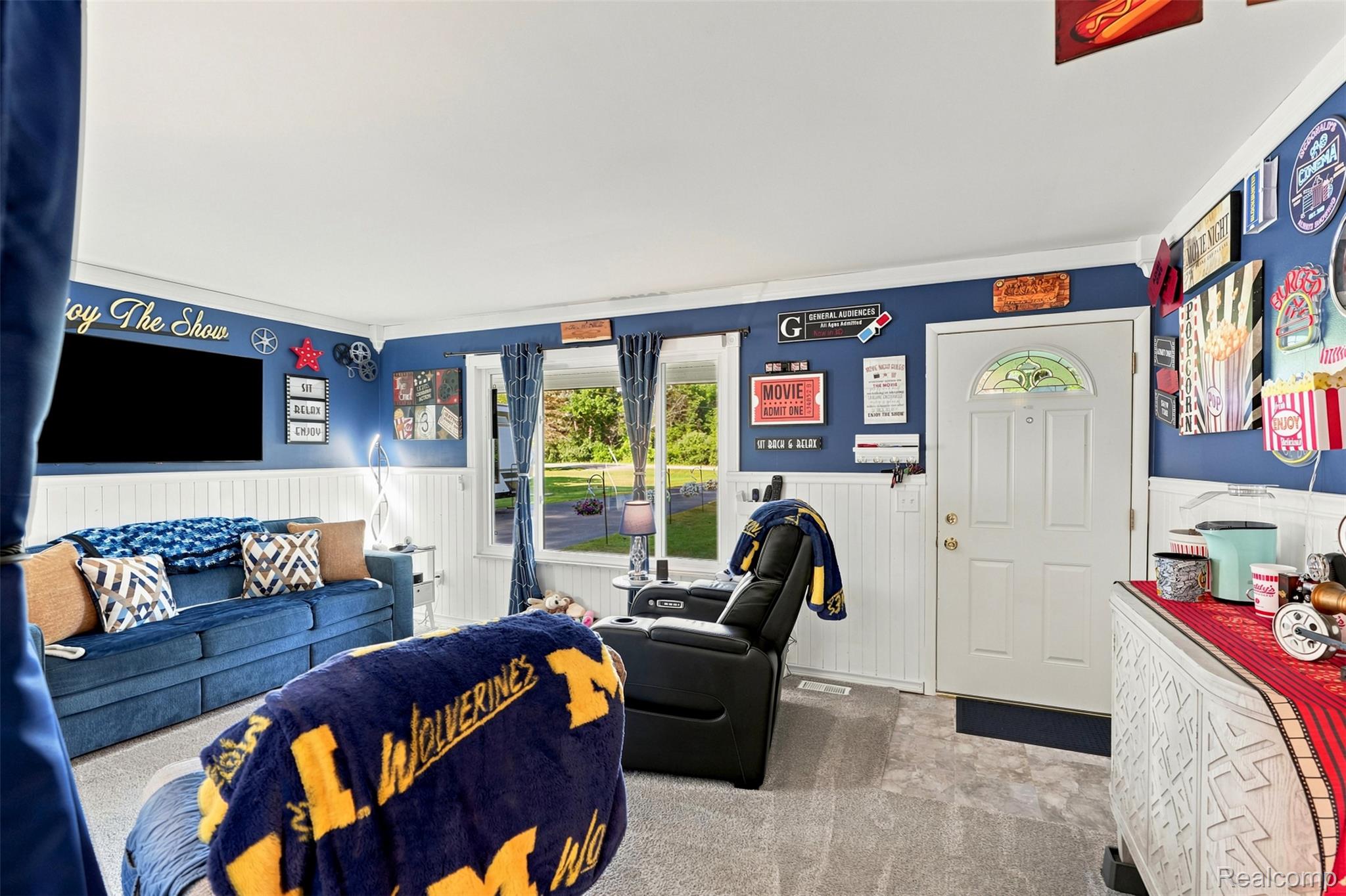 Living room featuring a paneled entry door with an arched stained-glass insert, carpeted flooring, and white beadboard wainscoting