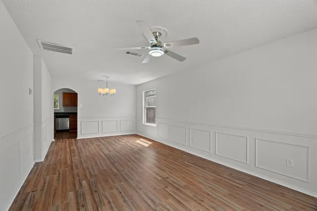 an empty room with wooden floor chandelier fan and windows