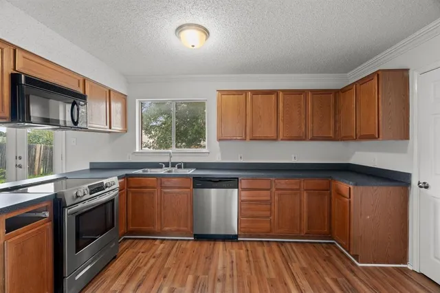 a kitchen with stainless steel appliances granite countertop wooden cabinets a sink a stove a refrigerator and dishwasher with wooden floor