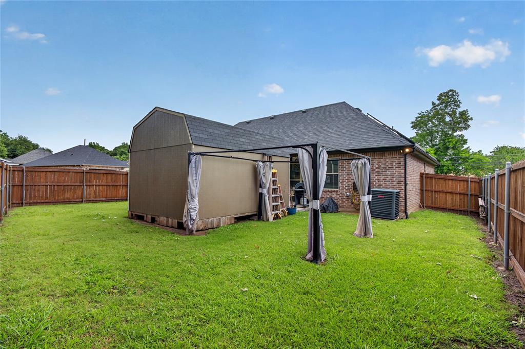 701 West Lamberth Road Sherman, TX 75092 - Photo 33 of 37 Expansive backyard featuring a manicured lawn, a privacy fence, a detached storage shed, a covered patio structure, and a brick-sided exterior