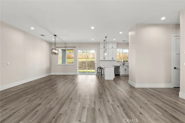 a view of an empty room and kitchen with wooden floor
