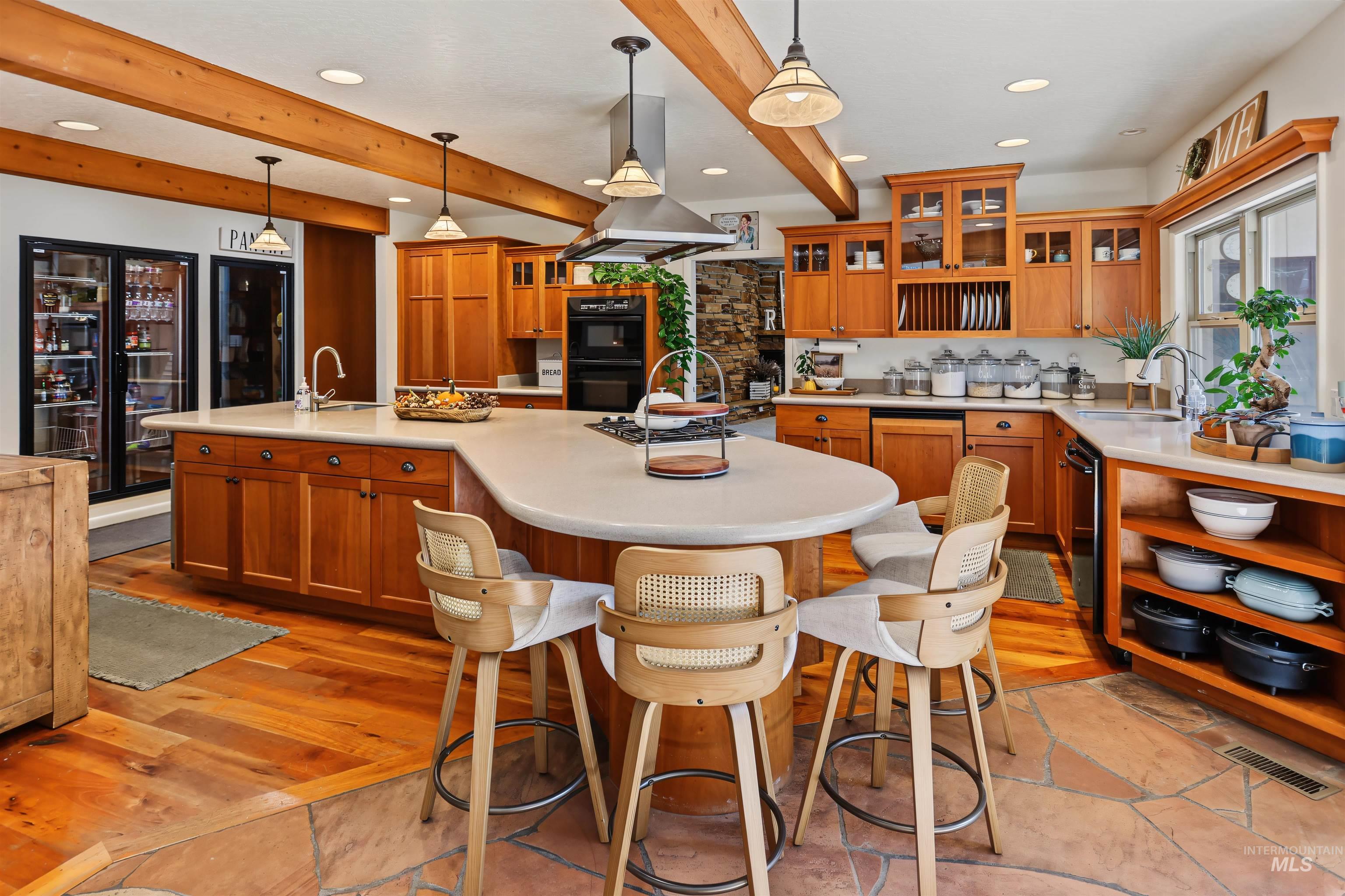508 East Elm Avenue Parma, ID 83660 - Photo 12 of 50 Spacious kitchen featuring exposed wood beams, wood-finish flooring, custom wood cabinetry, a large kitchen island with seating, and a built-in double oven