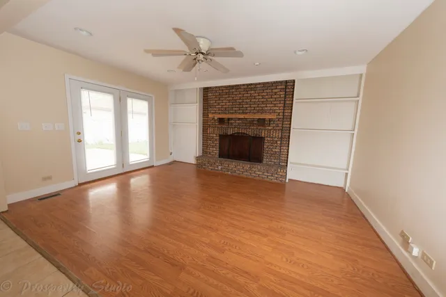 an empty room with wooden floor fireplace and windows