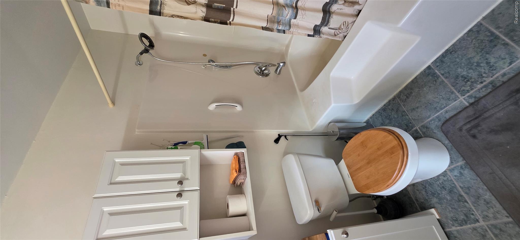 14062 Sanford Road Addison, MI 49220 - Photo 23 of 61 Bathroom featuring a white toilet with a wood-finish seat, a white tub-shower combination with a textured step, wall-mounted white cabinetry, and gray tile flooring
