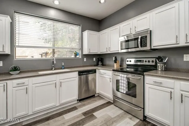 a kitchen with stainless steel appliances granite countertop white cabinets a sink and a window
