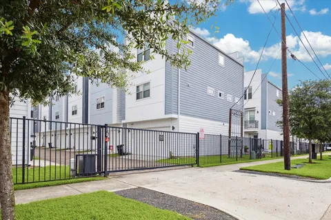 a view of a brick house in front of a yard with plants and large trees
