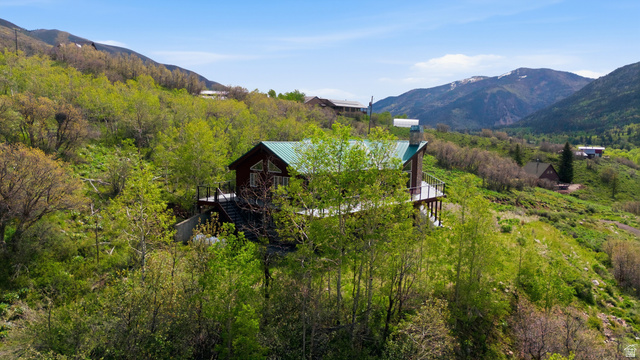6 Beaver Springs Rancheros Oakley, UT 84055 - Photo 51 of 68 Cabin-style residence featuring a dark wood exterior, a green metal roof, a prominent stone chimney, and a multi-level deck