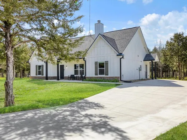 a view of a white house next to a yard with big trees