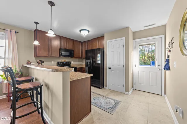 a kitchen with stainless steel appliances granite countertop a refrigerator a sink dishwasher a stove and a dining table with wooden floor