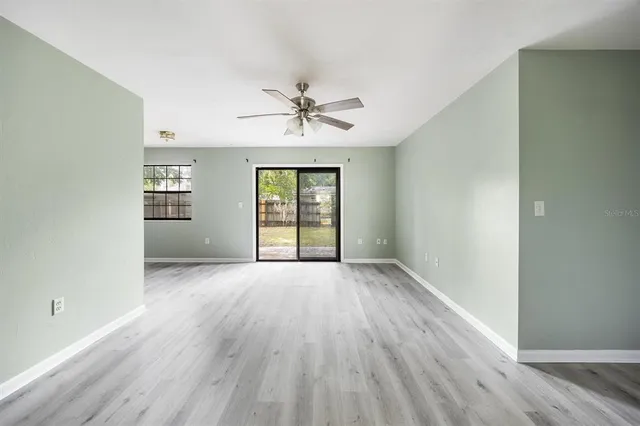 an empty room with wooden floor chandelier fan and windows