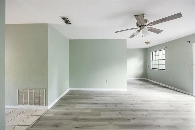 a view of an empty room with wooden floor and a ceiling fan