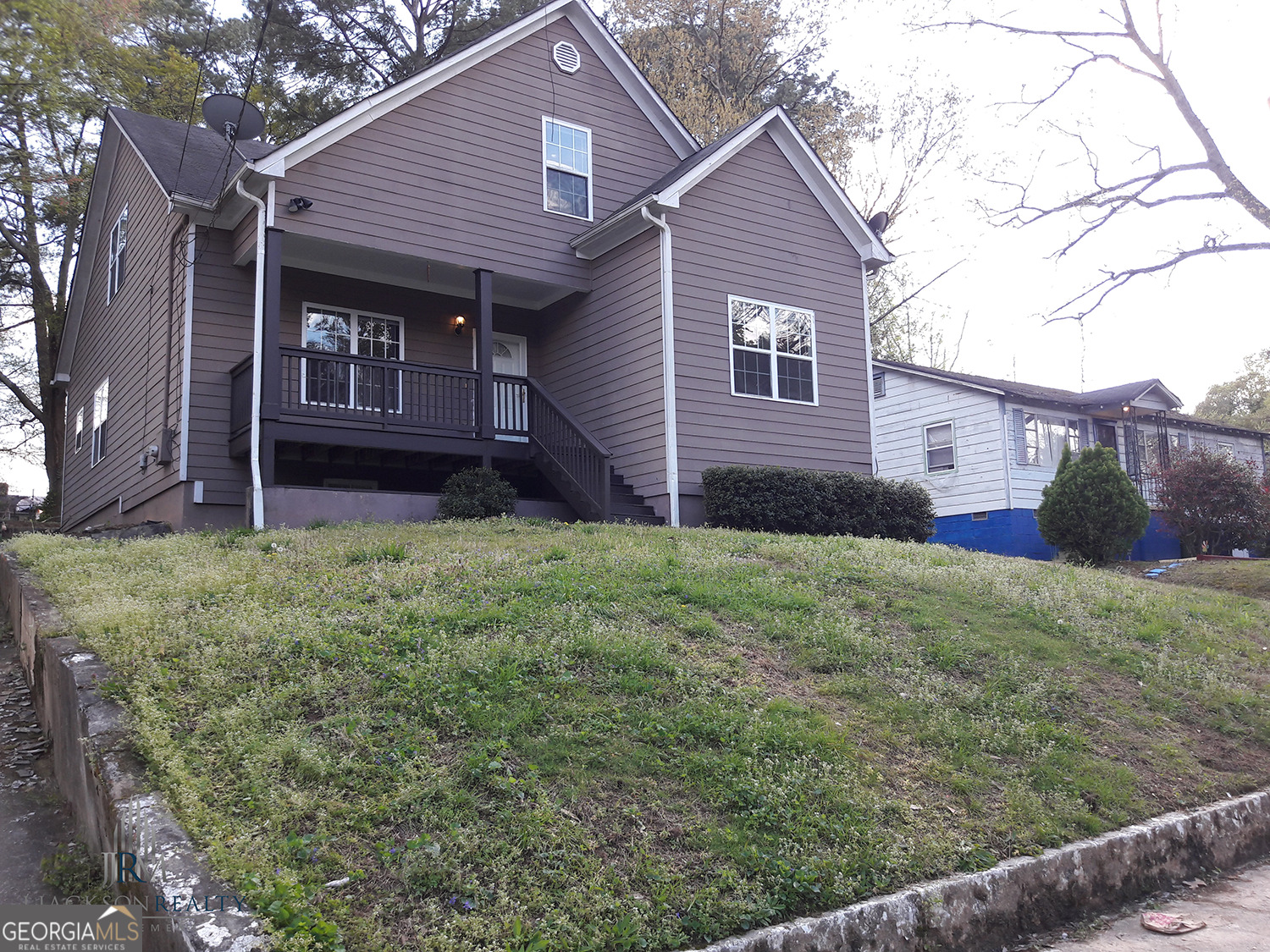 a view of a house with a yard plants and large tree