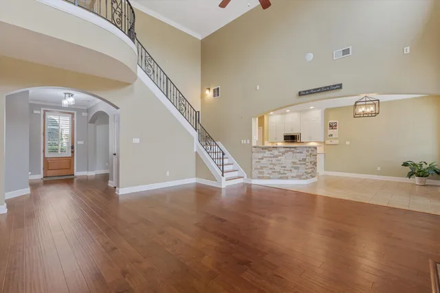 an empty room with chandelier fan and wooden floor
