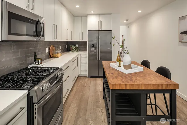 a kitchen with stainless steel appliances granite countertop a stove top oven a sink a dining table and chairs with wooden floor