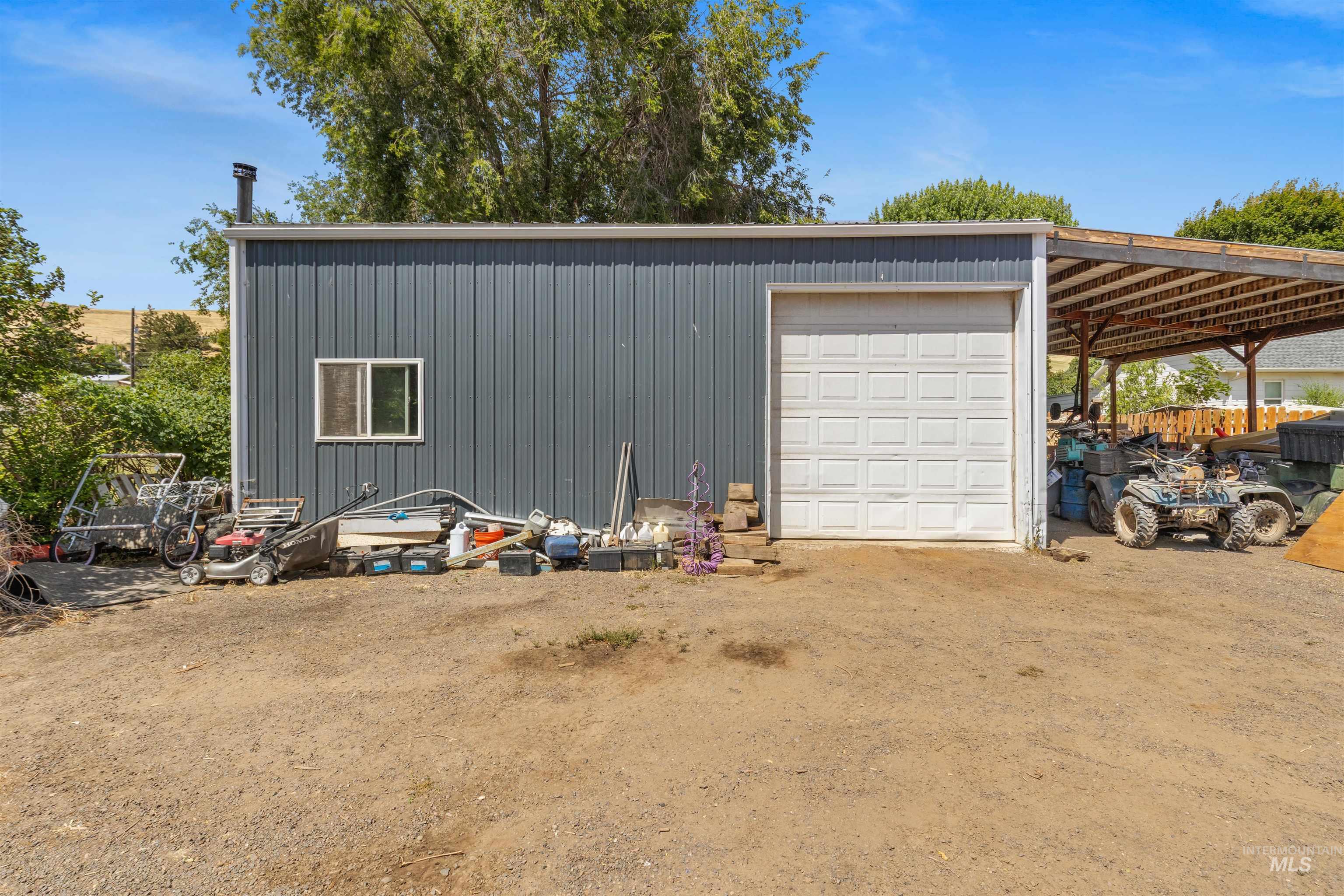 2460 State Street Pomeroy, WA 99347 - Photo 2 of 18 Metal-sided utility building featuring a white panel garage door, an awning-covered carport, and a single window