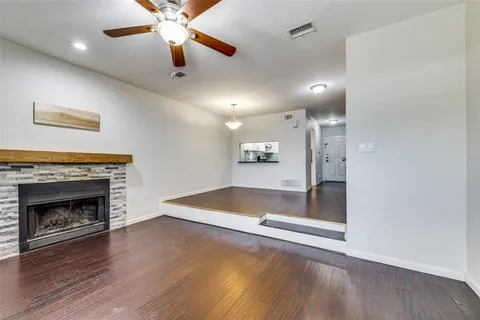 an empty room with wooden floor a ceiling fan a fireplace and windows