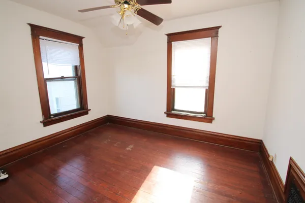 an empty room with wooden floor chandelier fan and windows