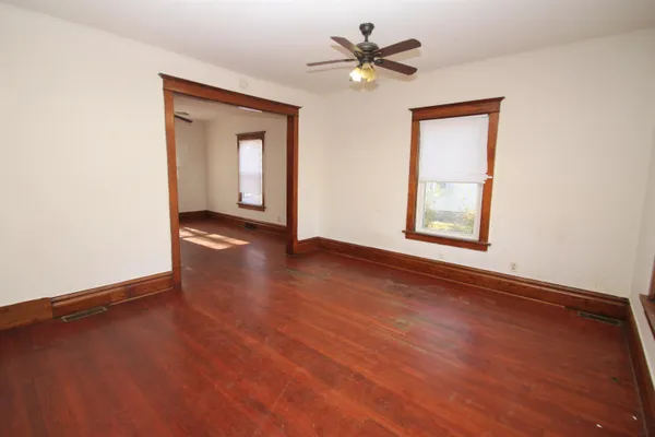 an empty room with wooden floor chandelier fan and windows