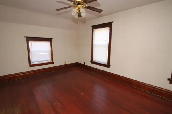 an empty room with wooden floor chandelier fan and windows