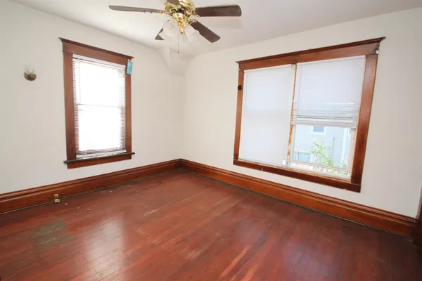 an empty room with wooden floor fan and windows