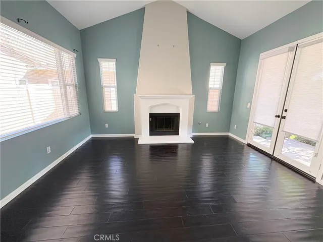 an empty room with wooden floor fireplace and windows