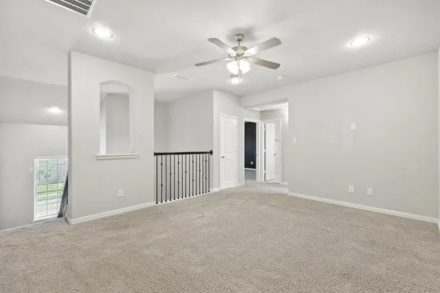 a view of an empty room with wooden floor and fan