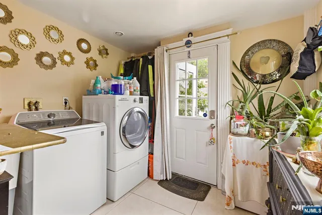 a view of a white house next to a yard with big trees and plants