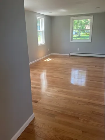 a view of an empty room with window and hardwood floor