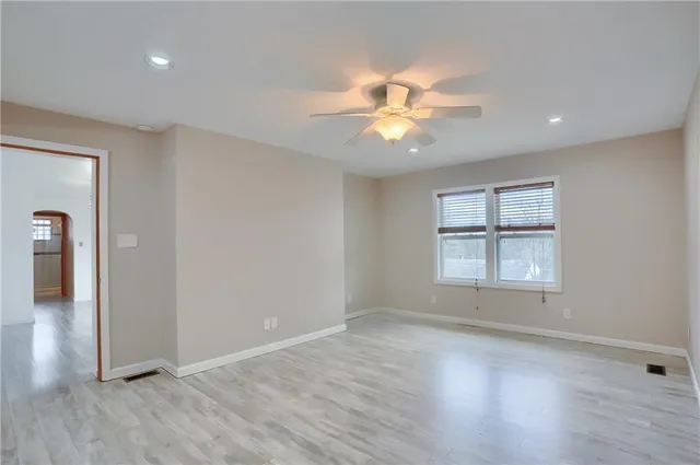 an empty room with wooden floor fan and windows
