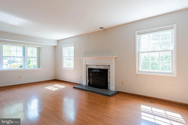 an empty room with wooden floor fireplace and windows