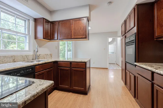 a kitchen with stainless steel appliances granite countertop wooden cabinets a stove top oven a sink and dishwasher with wooden floor