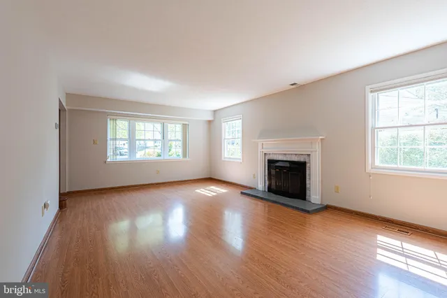 an empty room with wooden floor fireplace and windows