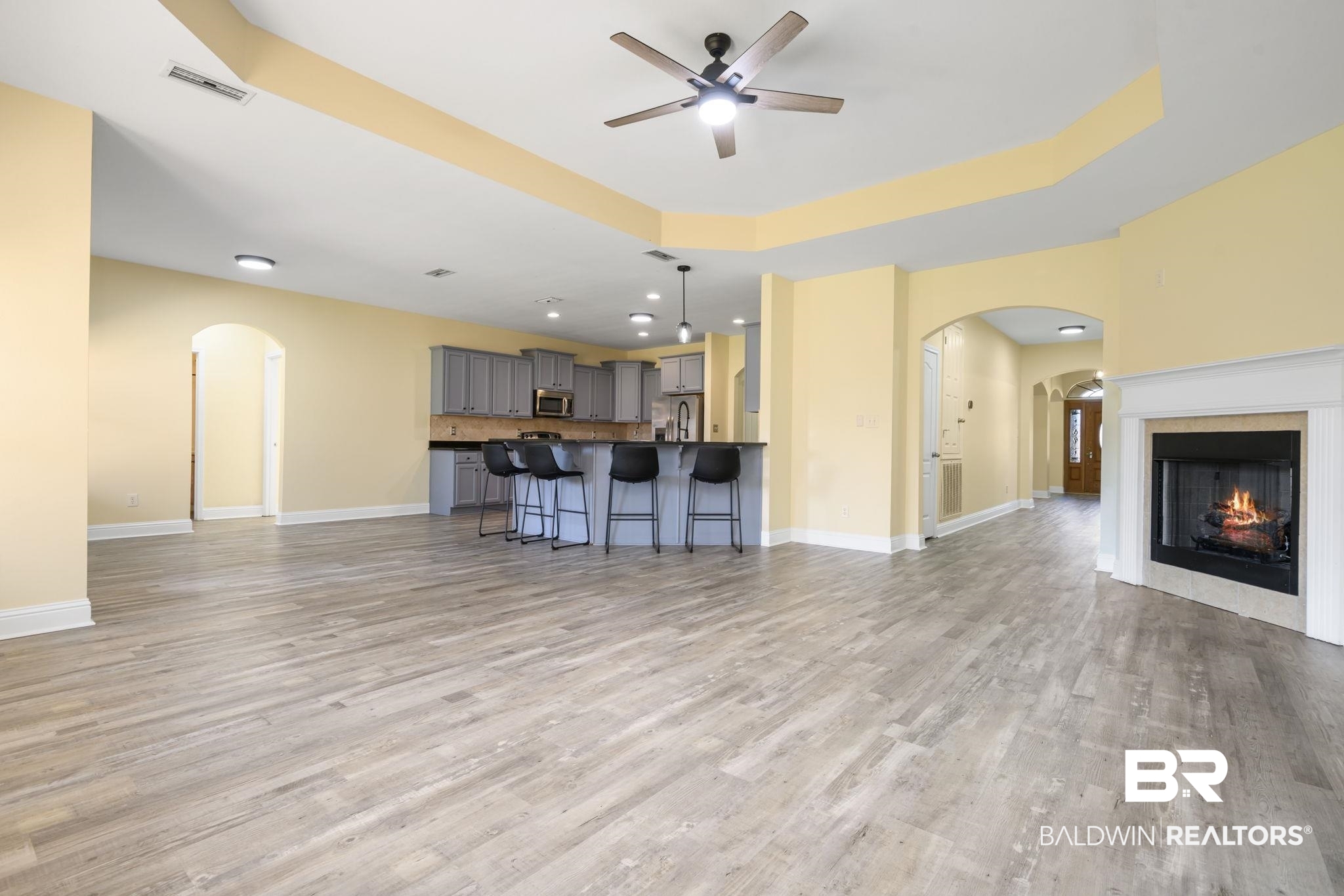 25234 Fairfax Road Daphne, AL 36526 - Photo 18 of 45 Unfurnished living room with arched walkways, ceiling fan, a raised ceiling, a warm lit fireplace, and light wood-style floors