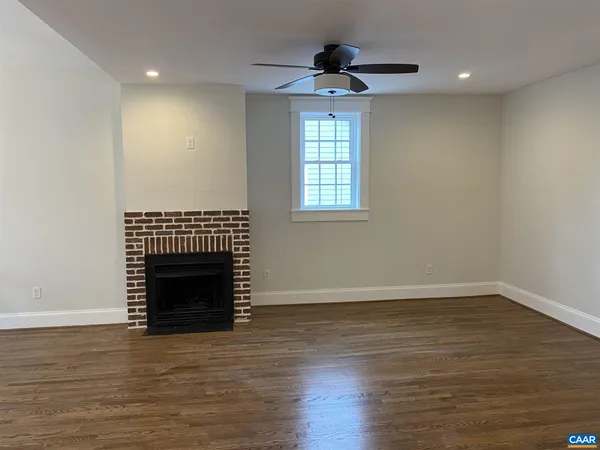 a view of an empty room with wooden floor fireplace and a window