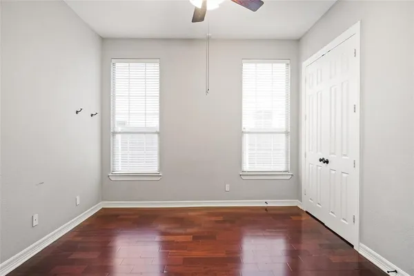 an empty room with wooden floor chandelier fan and windows