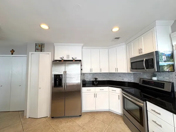 a kitchen with stainless steel appliances granite countertop a refrigerator a stove a sink and white cabinets