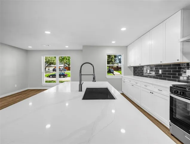 a large white kitchen with stainless steel appliances granite countertop a stove a sink a refrigerator white cabinets and a dining table