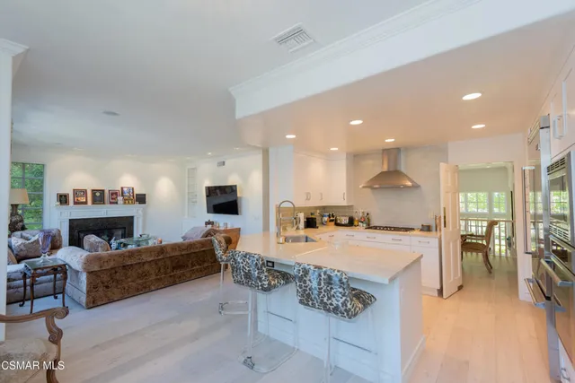 a large living room with stainless steel appliances kitchen island granite countertop a stove a sink a refrigerator and a dining table with wooden floor