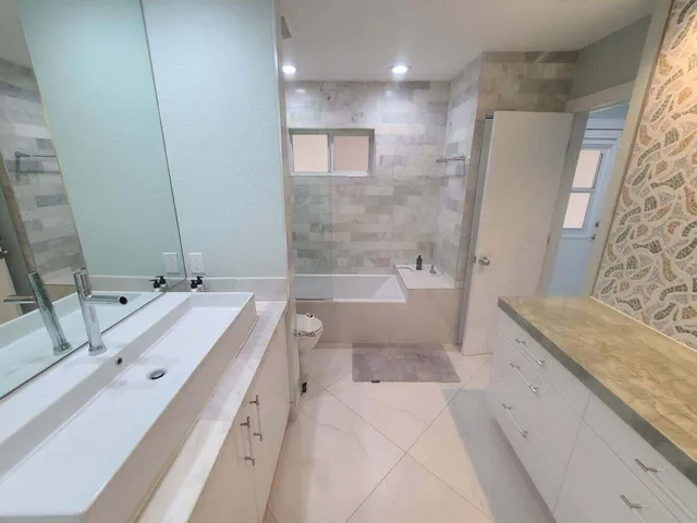 a bathroom with a granite countertop double vanity sink mirror bathtub and shower
