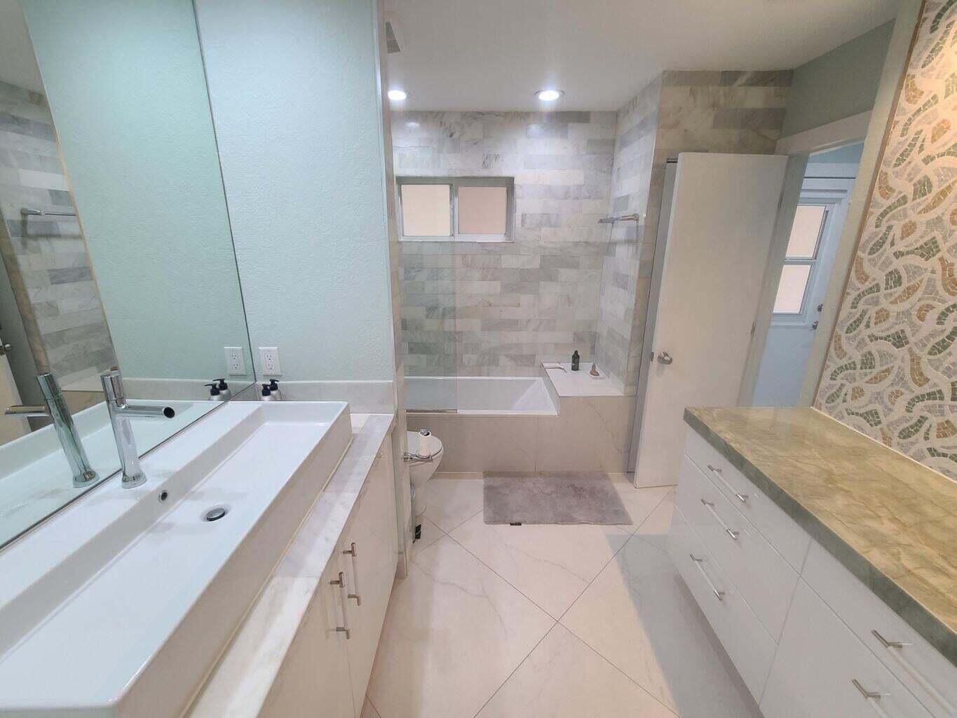 3851 North Ocean Boulevard, Unit 409 Gulf Stream, FL 33483 - Photo 16 of 29 a bathroom with a granite countertop double vanity sink mirror bathtub and shower