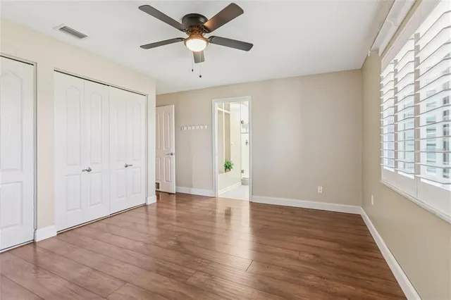 an empty room with wooden floor chandelier fan and windows