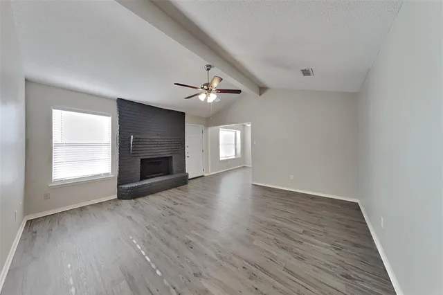 an empty room with wooden floor fireplace and windows