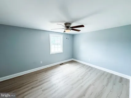an empty room with wooden floor fan and windows