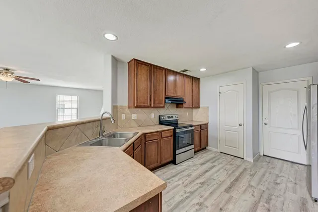 a kitchen with stainless steel appliances granite countertop wooden cabinets a stove a sink and dishwasher with wooden floor